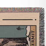 Close-up of a woven blanket with colorful fringe, featuring a design and text.
