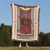 Person holding a 'Justice' tarot card blanket outdoors with trees and blue sky in the background