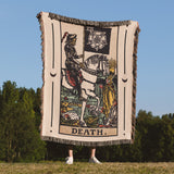Person holding a 'Death' tarot card blanket outdoors with trees and blue sky in the background