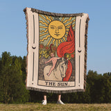 Person holding a blanket with 'The Sun' design in a field