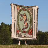 Person holding a tarot card-style blanket with 'The World' card design outdoors.