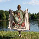 Person holding a 'The World' tarot card blanket by a lake