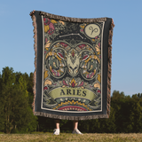 Person holding a decorative blanket with Aries zodiac design against a natural background