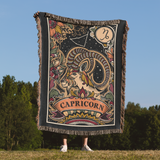 Person holding a Capricorn-themed blanket with astrological design against a natural background