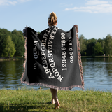 Person holding a black Ouija board-themed blanket by a lake