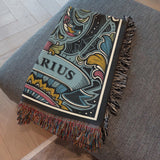 Decorative "Aquarius" blanket with intricate patterns draped over a gray surface.