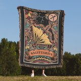 Person holding a blanket with Sagittarius zodiac design against a natural background