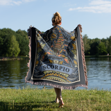 Person wearing a 'Scorpio' themed blanket by a lake