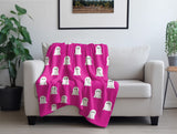 Pink blanket with ghost pattern draped over a white armchair in a room with plants and a framed picture.