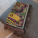 Colorful patterned blanket with fringe on a gray surface
