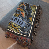 Decorative blanket with 'Scorpio' design on a gray couch.